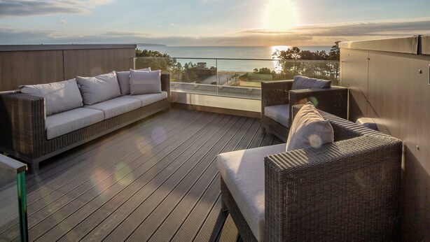 A rooftop terrace with a sofa and chairs, overlooking a body of water and a sunset. - Sky suite with unobstructed sea view, roof terrace and balcony (Ostseebad Binz)