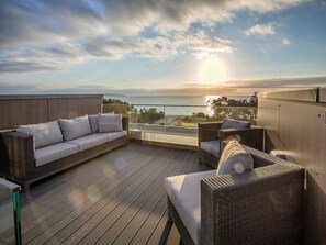 A rooftop terrace with a sofa and chairs, overlooking a body of water and a sunset. - Sky Suite with unobstructed ocean views, a rooftop terrace, and a balcony (Ostseebad Binz)