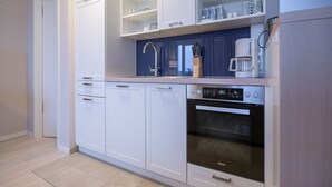 A modern kitchen with white cabinetry, a built-in oven, and a coffee maker. - Sky suite with unobstructed sea view, roof terrace and balcony (Ostseebad Binz)