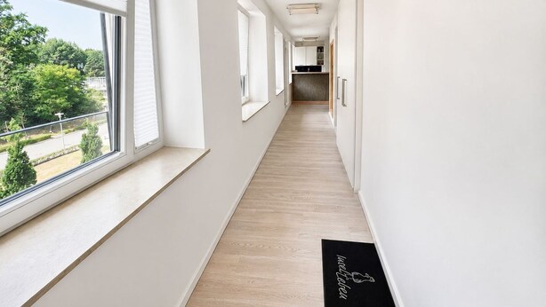 A corridor with large windows, a wooden floor, and a black doormat with text. - Apartment with sea view, 1 bedroom and balcony (Ostseebad Binz)