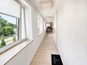 A corridor with large windows, a wooden floor, and a black doormat with text.