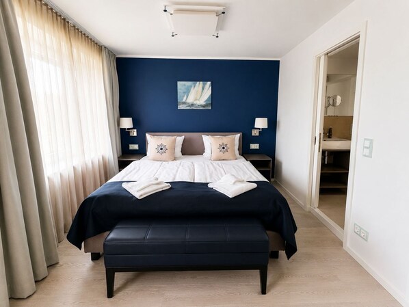 A bedroom with a bed, bedside lamps, a painting, and a view into the bathroom.