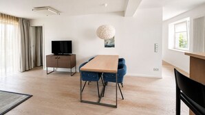 A modern living room with a wooden dining table, blue chairs, a flat-screen TV, and a large decorative light fixture. - Apartment with sea view, 1 bedroom and balcony (Ostseebad Binz)