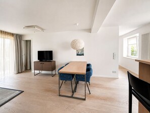 Un salon moderne avec une table à manger en bois, des chaises bleues, un téléviseur à écran plat et un grand luminaire décoratif.