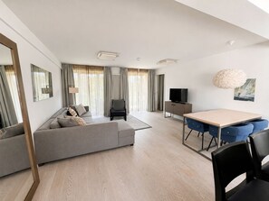 Ein modernes Wohnzimmer mit einer Couch, einem Esstisch mit Stühlen, einem Fernseher und einem Gemälde an der Wand.