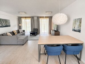 A modern living room with a grey sofa, a wooden dining table with blue chairs, and a large white pendant light.