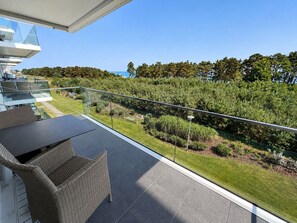A balcony with outdoor furniture, a glass railing, and a view of a landscaped garden and trees.