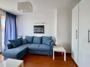 A modern living room with a blue sectional sofa, a white side table, and a cityscape artwork on the wall.