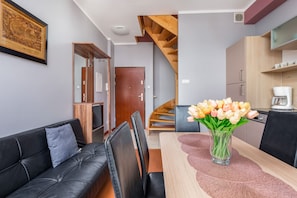 A modern living room with a black leather sofa, a dining table with a vase of tulips, and a staircase leading to an upper floor.