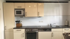 A modern kitchen with white cabinets, a microwave, a stove, and a dishwasher. - Duplex apartment in a conservation area (Solingen)