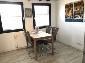 A dining area with a wooden table and four wicker chairs, a vase with flowers, and a wall clock. - Duplex apartment in a conservation area (Solingen)