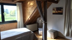 A bedroom with a wooden ceiling, a bed, a radiator, a window, and a fan. - Duplex apartment in a conservation area (Solingen)