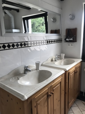 A bathroom with two sinks, wooden cabinets, a mirror, and a window with a view of trees. - Duplex apartment in a conservation area (Solingen)