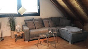 A cozy loft-style room with a wooden ceiling, a grey sofa with multiple cushions, a small glass table with two glasses, and a potted plant. - Duplex apartment in a conservation area (Solingen)