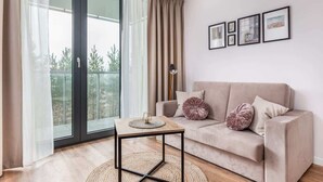 A modern living room with a sofa, a coffee table, and a view through a sliding glass door to an outdoor balcony. - Seaside Studio with Balcony | 50 m to the Beach | Parking (Mielno)