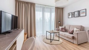 A modern living room with a flat-screen TV, a sofa, a coffee table, and a large window with curtains. - Seaside Studio with Balcony | 50 m to the Beach | Parking (Mielno)