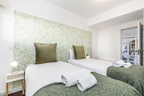 Ein Hotelzimmer mit zwei Betten, grüner Bettwäsche, einer Nachttischlampe und einem Schrank mit Regalen.