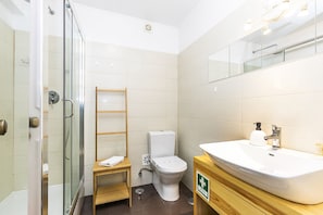 Ein modernes Badezimmer mit einer Duschkabine aus Glas, einer Toilette, einem Holzboden und einem Waschbecken mit Spiegel darüber.