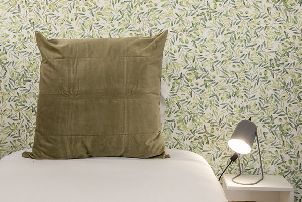 A bed with a single green pillow and a bedside table with a lamp.