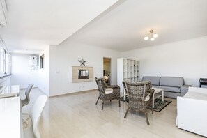 A modern living room with a grey sofa, wicker chairs, a white coffee table, and a bookshelf.