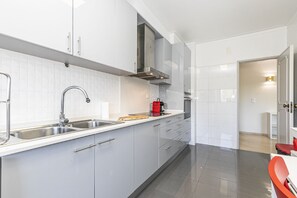 Eine moderne Küche mit weißen Schränken, Edelstahlgeräten und einem roten Wasserkocher auf der Arbeitsplatte.