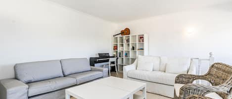 Ett vardagsrum med en grå soffa, en vit soffa, ett vitt soffbord, flätade stolar, en bokhylla och en taklampa.
