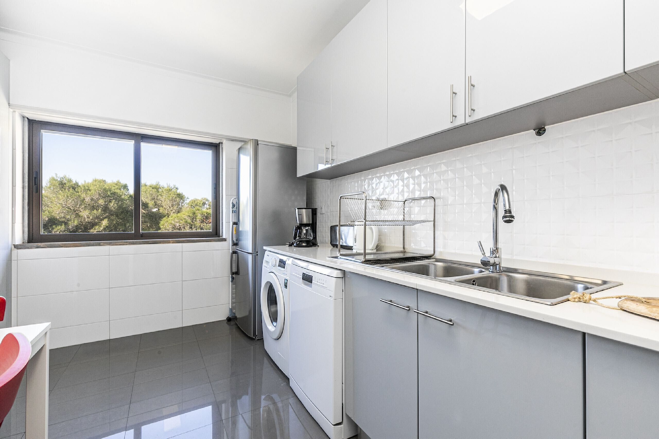 Cocina moderna con lavadora, cafetera y lavamanos.