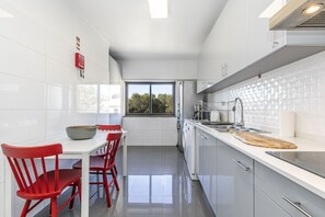 A modern kitchen with white cabinets, a dining table with red chairs, and a large window providing natural light.
