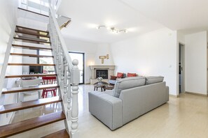 A spacious living area with a grey sofa, wooden staircase, and a fireplace.
