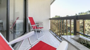 En balkon med glasdør, en rød stol og et hvidt bord.