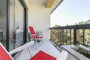 Un balcón con puerta de cristal, una silla roja y una mesa blanca.