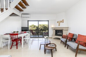 A spacious living area with a dining table, red chairs, a grey sofa, and a fireplace.