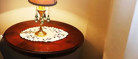 Una esquina con una mesa de madera, una lámpara encendida y una cesta de mimbre con libros.