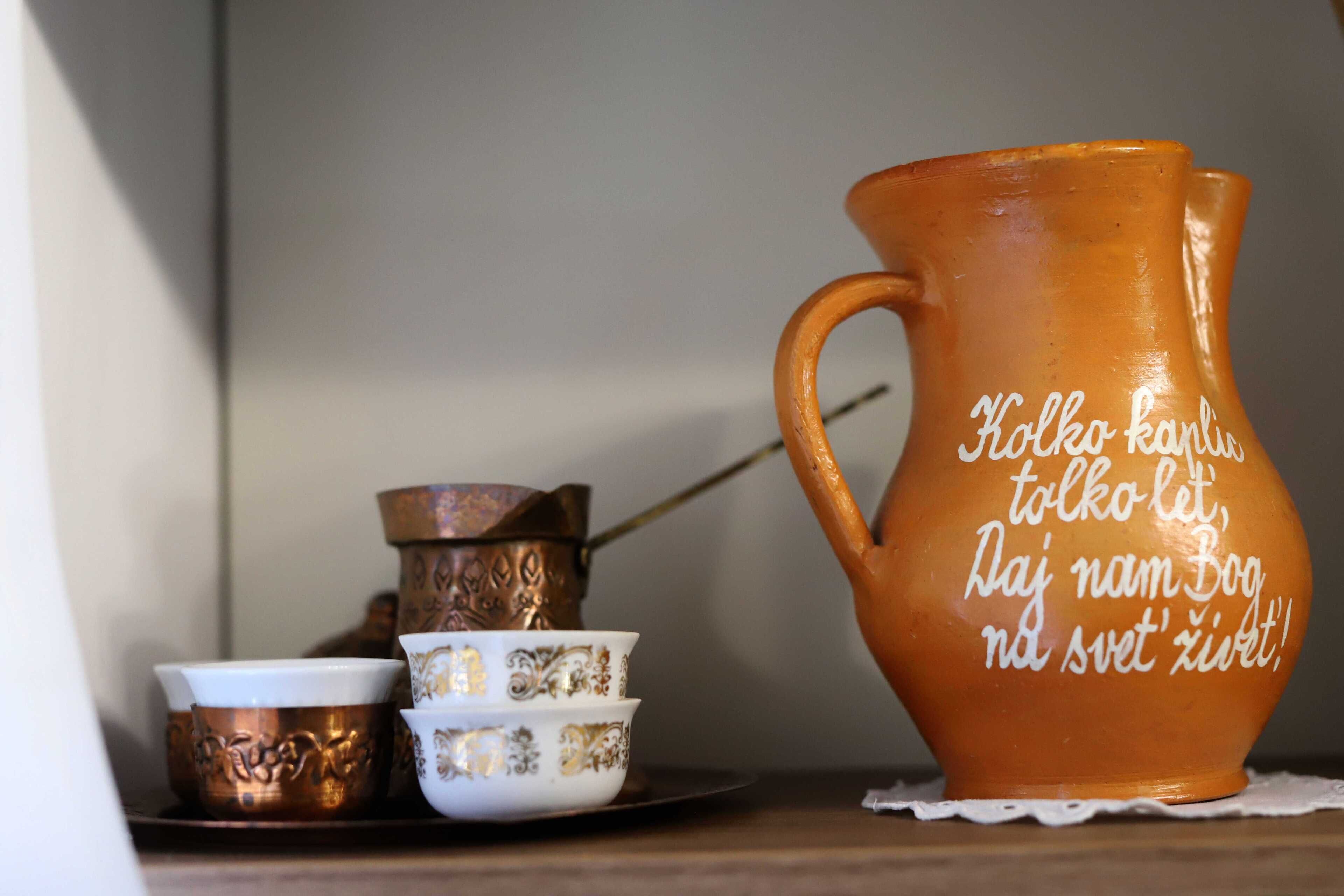 Una jarra de cerámica con texto, una olla de cobre y dos tazas a juego sobre una superficie de madera.