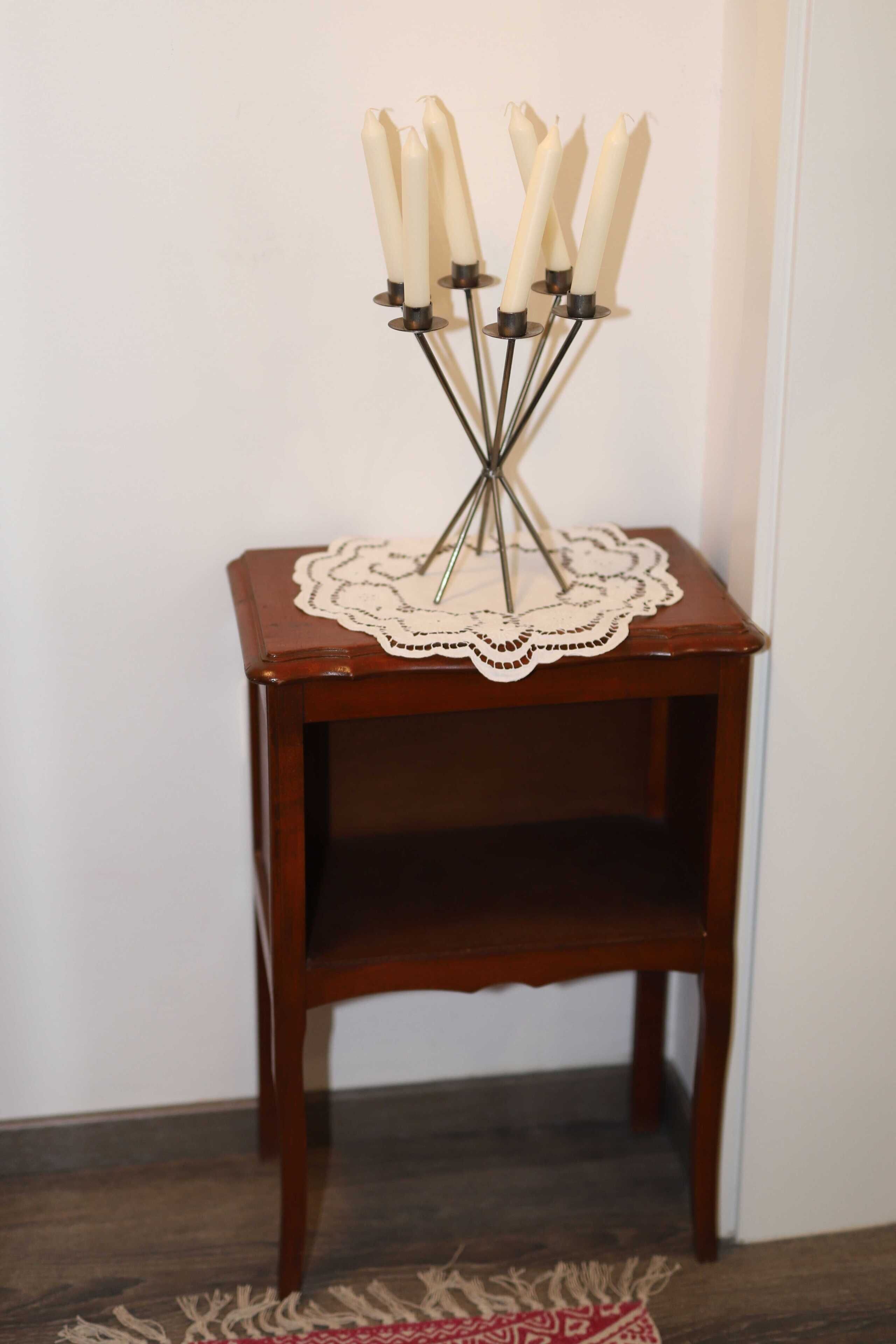 A small wooden side table with a lace doily and a candle holder with white candles.