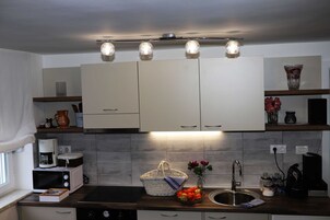 Una cocina moderna con armarios blancos, microondas, cafetera y una cesta de fruta.
