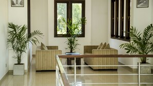 A modern living room with a sofa set, a coffee table, and two potted plants. There is a large window with a view of greenery outside. - Villa Upper Dickson (Galle)
