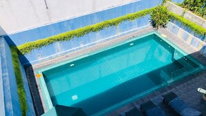 A rectangular swimming pool with a tiled deck, surrounded by a low wall with greenery. There are lounge chairs and an umbrella on the deck. - Villa Upper Dickson (Galle)