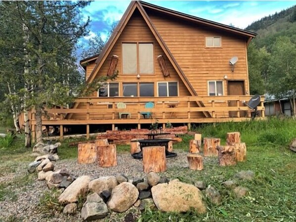 Escape to a serene cabin surrounded by lush greenery, featuring a central entrance and wooden deck with seating.