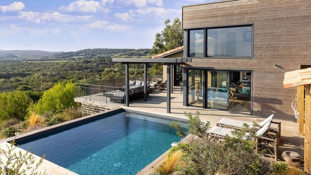 Et moderne hus med swimmingpool, udendørs møbler og udsigt over landskabet.