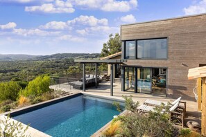 Ein modernes Haus mit Swimmingpool, Sitzgelegenheiten im Freien und Blick auf die Landschaft.