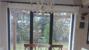 A dining area with a wooden table and chairs, a chandelier, and large windows with a view of trees.