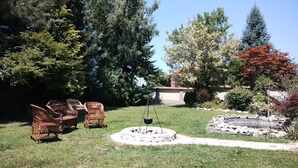 A backyard with a fire pit, wicker chairs, and a variety of trees.