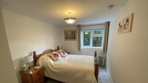 Une chambre à coucher comprenant un lit, une table de chevet, une commode, une fenêtre donnant sur un espace verdoyant et un radiateur.