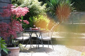 An outdoor patio with a round table and two chairs, surrounded by potted plants and a small pond. - Self Catering Private Annex Near Ferndown (Ferndown)