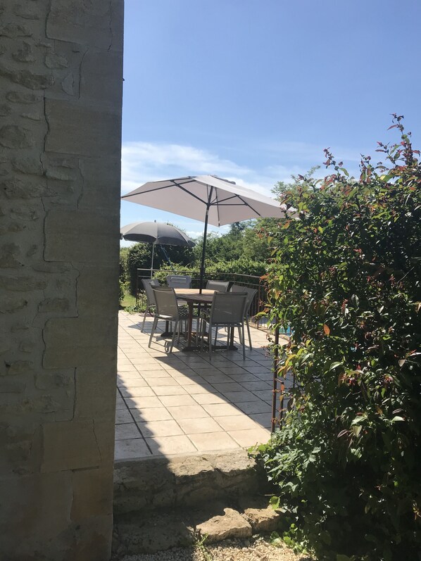 A patio with a table and chairs, two umbrellas, and a stone wall.