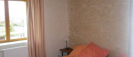 Une chambre avec deux lits en bois, une fenêtre avec des rideaux, une table de chevet et un mur en pierre.