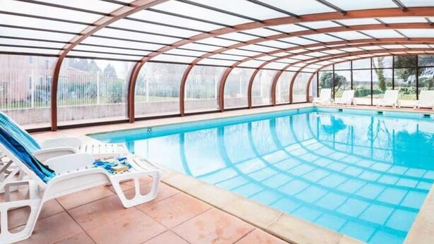 Una piscina interna con struttura a tetto curvo, pannelli di vetro trasparenti e poltrone a bordo vasca.