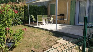 Un'area patio esterna con un tavolo e sedie, un tavolino con una sedia e un cancello verde.