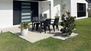 A modern house with a patio, a dining table with chairs, and a small garden.